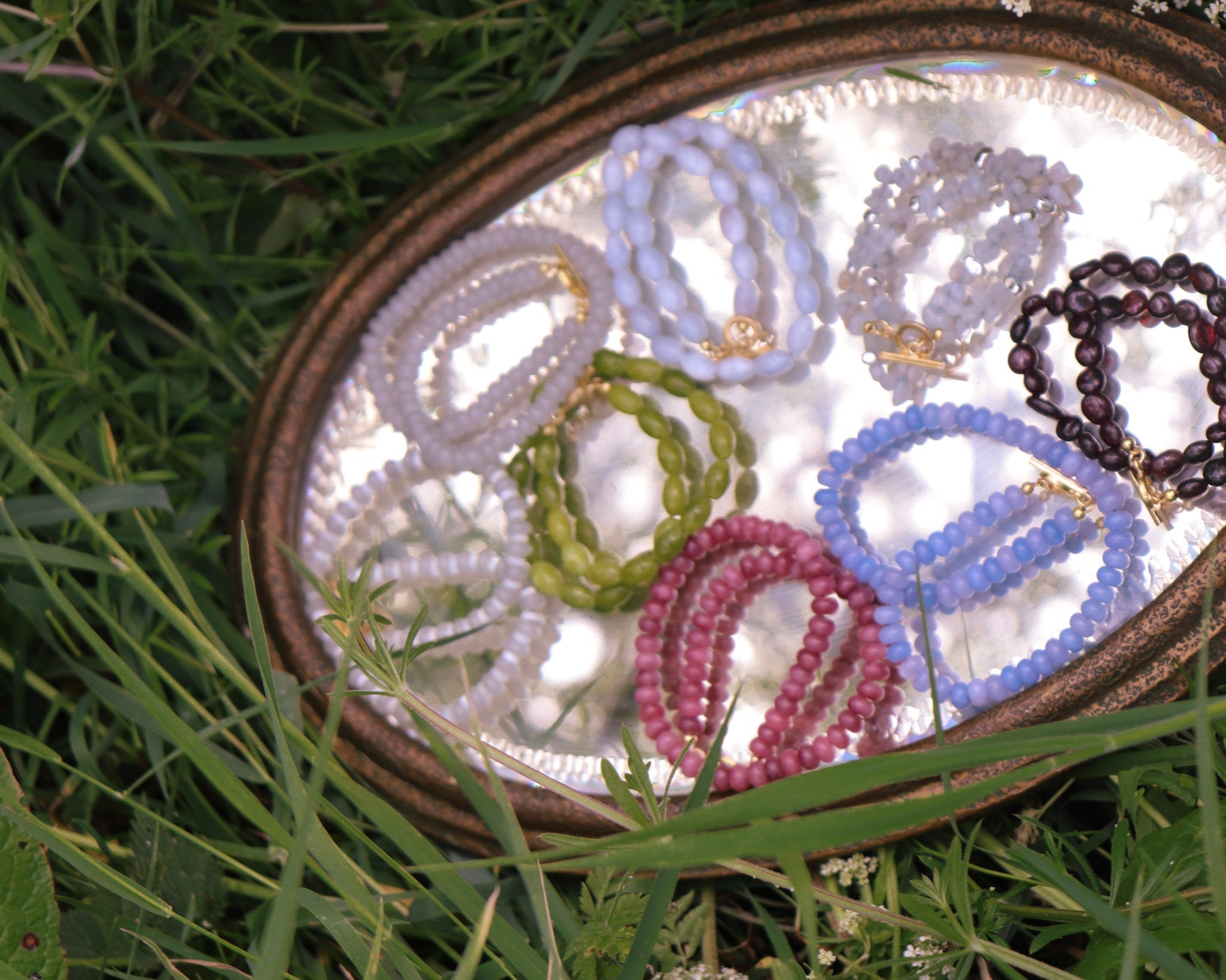Set of colorful beaded necklaces in a clear dish on grass